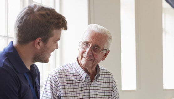 Senior man sitting looking at photo album with male nurse | Sunscape Boca Raton