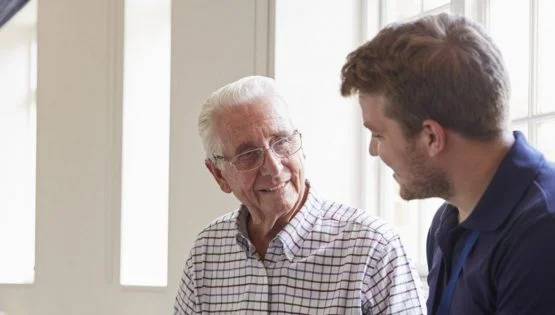 Retirement Community in Boca Raton, FL | Sunscape Boca Raton Senior man sitting looking at photo album with male nurse