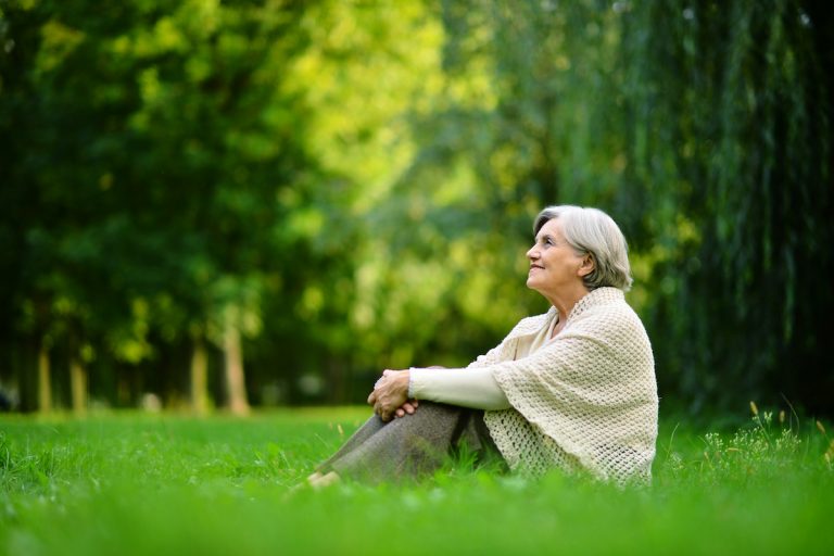 4 Benefits of Being Outdoors & Natural Light Therapy for Dementia Senior Woman Sitting on Grass_Light Therapy for Dementia