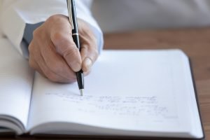 Senior Man Writing in Medical Journal_Physician Visits