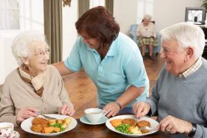 Couple of seniors being served their meal by a caregiver