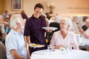 7 Vital Signs It’s Time for Assisted Living Female chef serving two older adults at a senior living community
