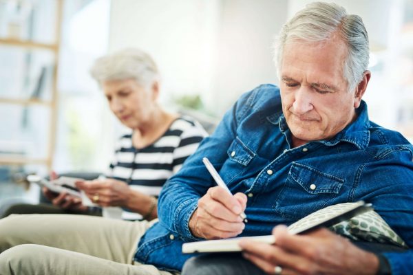 two older adults writing in notebook