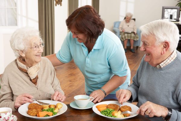 Couple of seniors being served their meal by a caregiver